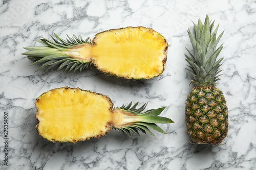 Fresh whole and cut pineapples on white marble background, top view