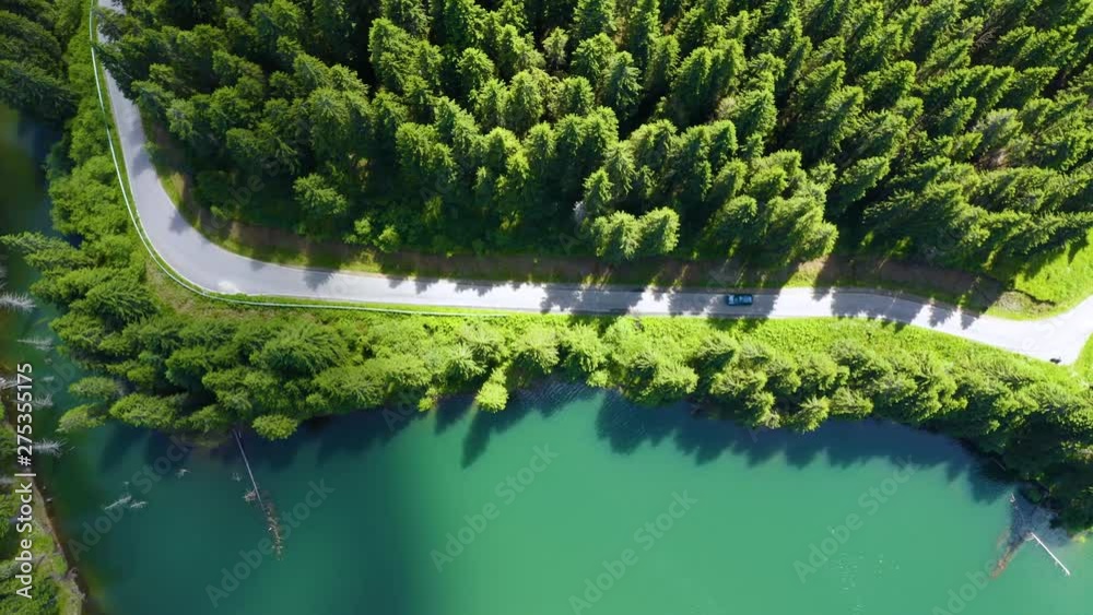 Aerial view of car driving through the fores and the lake on the side. Beautiful mountain road. Driving on the mountain road. Road trip. Mountain forest lake landscape. Car driving through pine forest