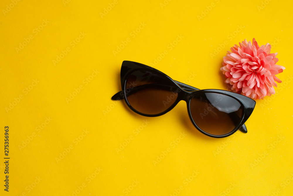 Woman sunglasses with flower on yellow background. Summer vacation concept.