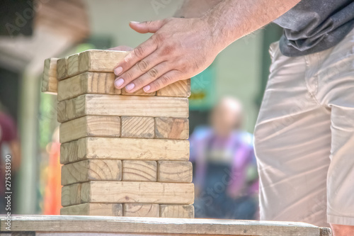 Cropped man straightens a Timber Tower Wood Block Stacking Game on a table with his hands - blurred people in background