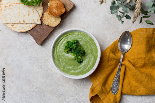 Broccoli cream soup, with bread, spoon and orange napkin on concrete background