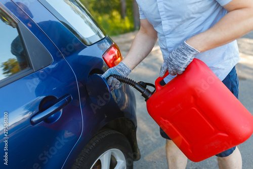 Wallpaper Mural Man pours fuel into the gas tank of his car from a red canister. Driver fills the fuel in an empty tank from a plastic canister. Young man stopped on the side of the road refills the car. Torontodigital.ca