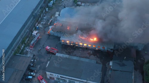 Aerial view a infernal fire in warehouse with big flame and smoke above the zone at dusk. Firemen in action to extinguish the fire in the warehouse zone. photo