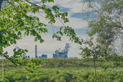 chimneys and cooling towers of a coal-fired power plant seen through green branches of trees, protection of air against pollution, restrictions on carbon dioxide emissions