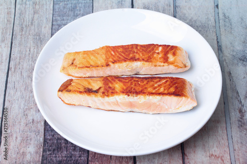 2 Grilled salmon steaks on white plate served on wood.