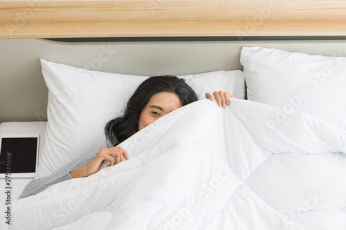 Woman lying in bed and looking over the blanket..