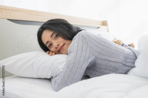 Asian woman lies on one's side on bed in bedroom..