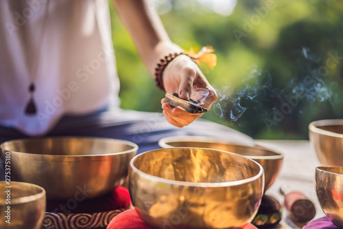 Woman playing on Tibetan singing bowl while sitting on yoga mat against a waterfall. Vintage tonned. Beautiful girl with mala beads meditating photo