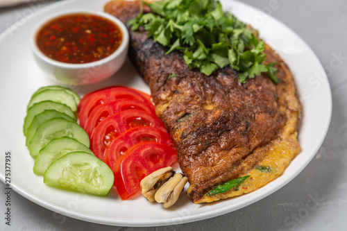 Omelet with mussels. Popular Thai food served with fresh vegetables and sauce on a plate.