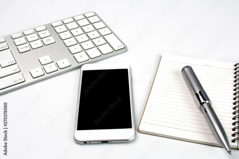 Smartphone,computer keyboard and notepad on white desk Smartphone,computer keyboard and notepad on white desk
