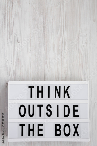 'Think outside the box' words on a lightbox on a white wooden surface, top view. Flat lay, overhead, from above. Copy space.