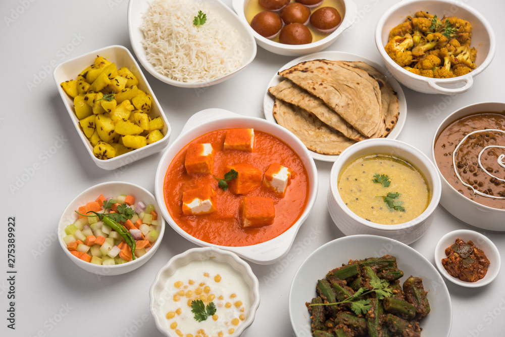 Assorted Indian food like paneer butter masala, dal, roti, rice, sabji, gulab jamun and bound raita served in bowls over moody background, selective focus Assorted Indian food like paneer butter masala, dal, roti, rice, sabji, gulab jamun and bound raita served in bowls over moody background, selective focus