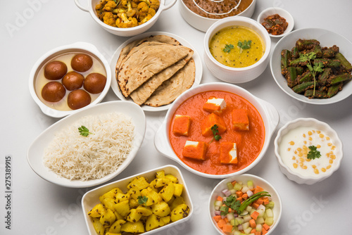 Assorted Indian food like paneer butter masala, dal, roti, rice, sabji, gulab jamun and bound raita served in bowls over moody background, selective focus