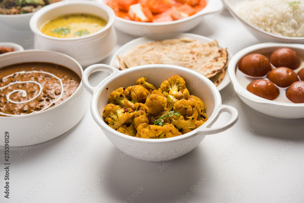 Assorted Indian food like paneer butter masala, dal, roti, rice, sabji, gulab jamun and bound raita served in bowls over moody background, selective focus Assorted Indian food like paneer butter masala, dal, roti, rice, sabji, gulab jamun and bound raita served in bowls over moody background, selective focus