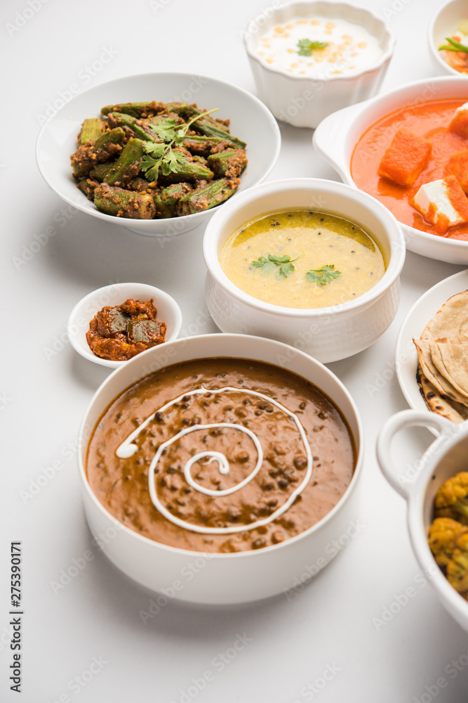 Assorted Indian food like paneer butter masala, dal, roti, rice, sabji, gulab jamun and bound raita served in bowls over moody background, selective focus Assorted Indian food like paneer butter masala, dal, roti, rice, sabji, gulab jamun and bound raita served in bowls over moody background, selective focus