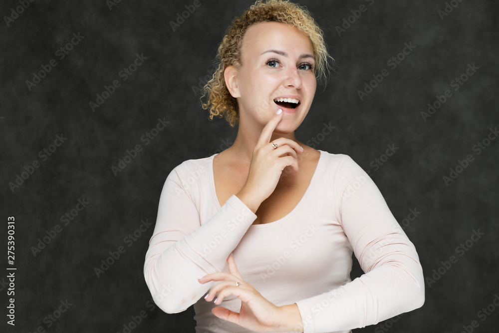 Photo portrait of a beautiful girl blonde woman with short curly hair on a dark gray background talking and showing a lot of emotions. Shows hands. Beauty. Made in a studio. Photo portrait of a beautiful girl blonde woman with short curly hair on a dark gray background talking and showing a lot of emotions. Shows hands. Beauty. Made in a studio.
