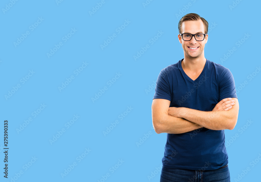 Fototapeta premium Portrait of young happy man wearing in glasses, casual smart blue clothing, with crossed arms, over blue background