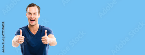 Photo of excited happy man in blue casual smart wear, showing thumbs up gesture, over blue color background