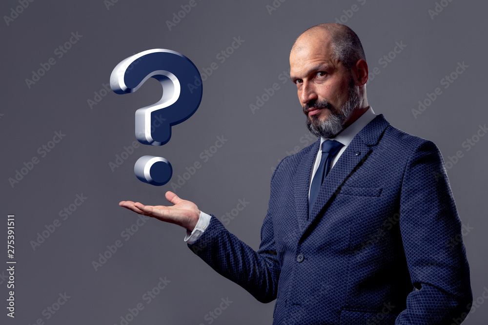Bald middle-aged man with a beard, in a jacket with a white shirt and blue tie, stretches out his hand to represent an object on a dirty gray background Bald middle-aged man with a beard, in a jacket with a white shirt and blue tie, stretches out his hand to represent an object on a dirty gray background