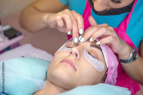 Woman stylist in the beauty salon is working on eyelash extension to the client. Process of working as a professional master for lengthening eyelashes