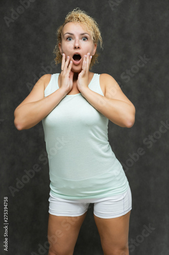 Photo portrait above the knee of a beautiful girl blonde woman with short curly hair on a gray background in bright linen is talking and showing a lot of emotions. An experienced model shows hands.