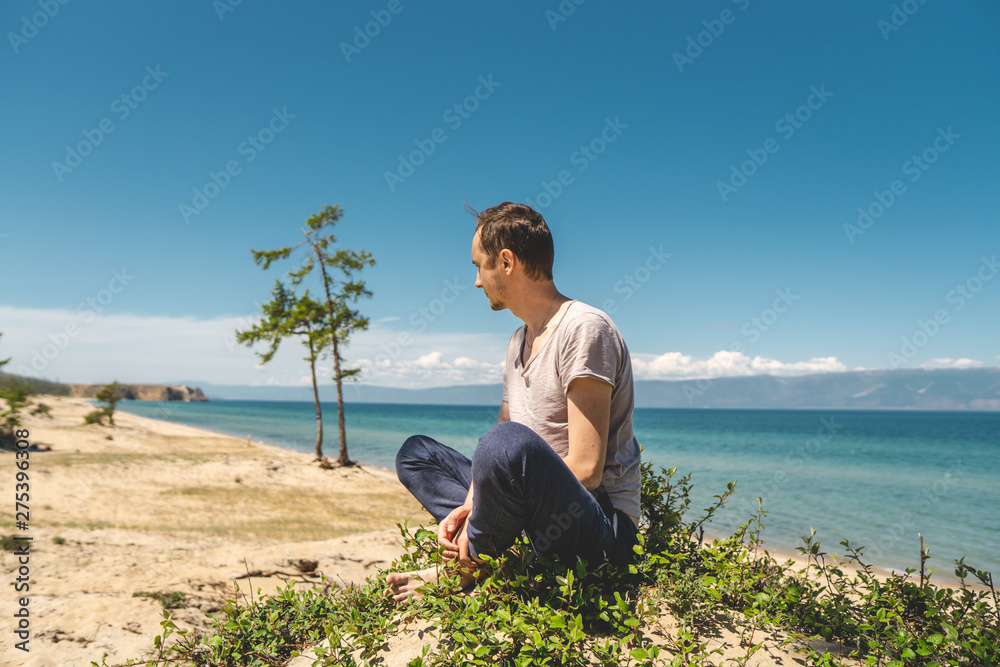 Man traveler relaxing on the beach of Olkhon island overlooking the water of the lake and the mountains and the blue sky