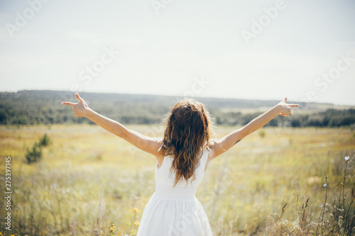 Happy girl in white dress stand in the field. Girl photo from the back. Concept of freedom, happiness, summer days. Horizontal stock photo.
