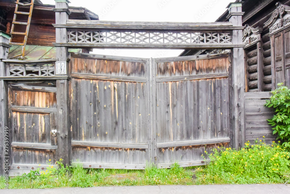 Old wooden fence with grass with green trees next to wooden house Old wooden fence with grass with green trees next to wooden house