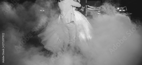 First wedding dance of a couple. Beautiful lights and luxury dress. Bride and groom in love hugging.