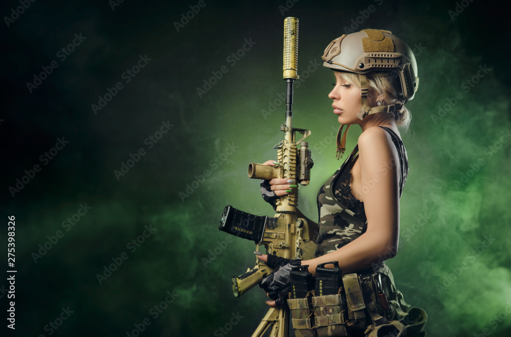 the girl in military overalls airsoft posing with a gun in his hands on a dark background in the haze - obrazy, fototapety, plakaty 