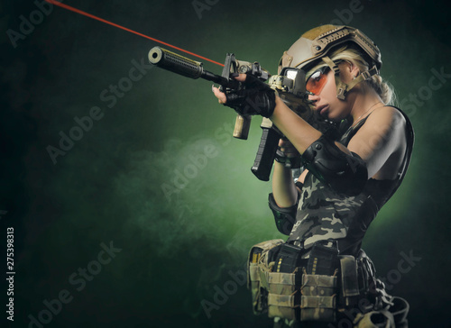 Fototapet the girl in military overalls airsoft posing with a gun in his hands on a dark b