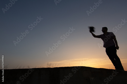 silhouette of man throwing hat at sunset