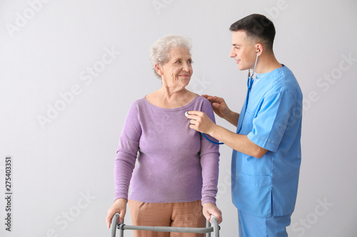 Young caregiver with senior woman on grey background