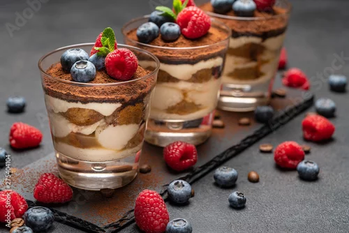 Obraz  z motywem Classic tiramisu dessert with blueberries and raspberries in a glass on stone serving board on dark concrete background