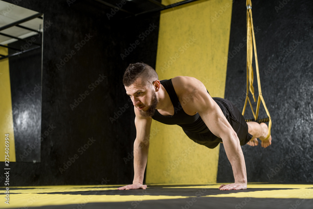 Muscular man does exercises with fitness straps in the gym with black and yellow interior - obrazy, fototapety, plakaty 