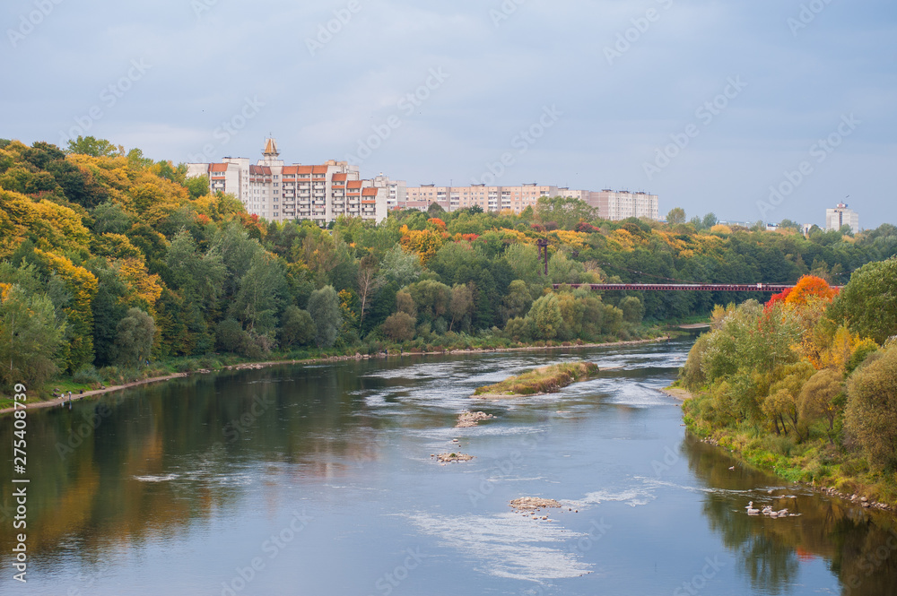 River on the background of the autumn forest and residential area. Forest river reflection autumn landscape. Autumn forest river water panorama. Forest river reflection in autumn