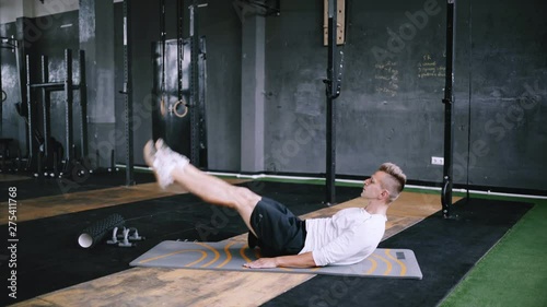 Man in good physical condition does flutter kicks to improve sports training in gym on yoga mat, best exercises for abs and core. Intermediate no equipmetn exersize to endurance. Calisthenics and