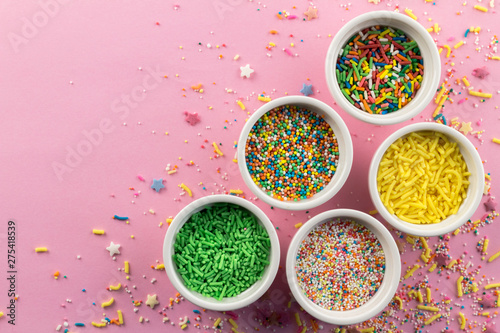 Cake sprinkles on pink background - Assorted colourful cake topping sprinkles in little white bowls on pink - top view