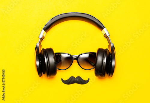 Creative party decoration concept. Black mustache, Sunglasses, headphones for music, props for photo booths carnival parties on yellow background top view flat lay. Father's day, Men's accessories