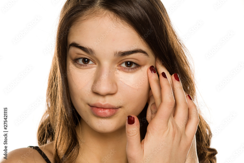 Young beautiful woman applying concealer with the fingers on white background Young beautiful woman applying concealer with the fingers on white background