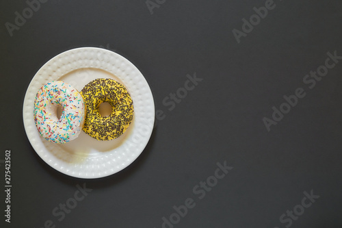 Glazed vanila donut on a plate on black stone background. Minimal flat lay with copy space 