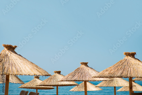 Fototapeta Naklejka Na Ścianę i Meble -  Straw beach umbrellas on a blue sky and sea background with a copy space. Travel, tourism, resort, summer vacation concept
