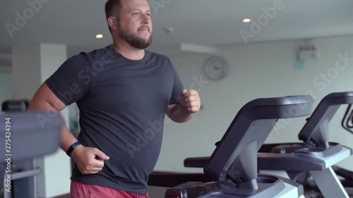 chubby man walking on running track, warming up on gym treadmill.