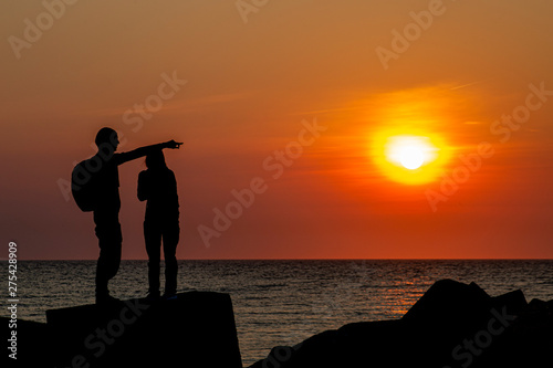 Silhouette of a young couple standing on the concrete pier protection blocks at Scheveningen under a vivid sunset moment, The Hague, Netherlands