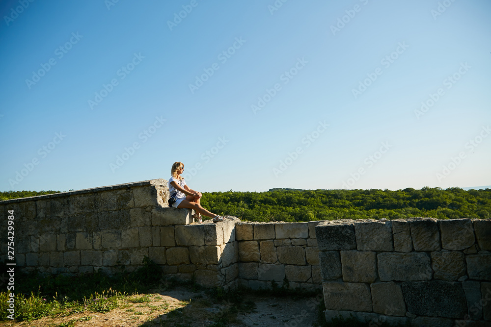 Fototapeta premium A woman sits on an ancient stone wall admiring the scenery of the Crimean peninsula.