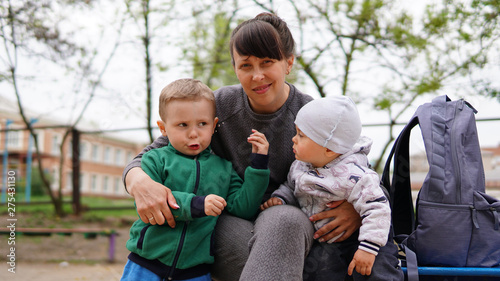 Happy mother and two little children posing together on playground in summer