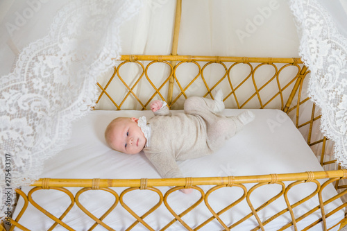 View of a  awake baby of 2 months in beige layette lying on his back in his crib. photo