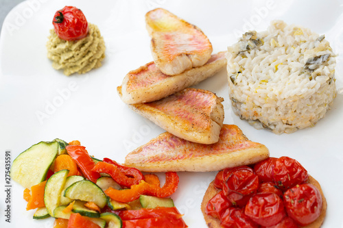 Presentation of a Mediterranean plate with fillets of red mullet, rice, tartlets with cherry tomatoes and colorful vegetables. photo