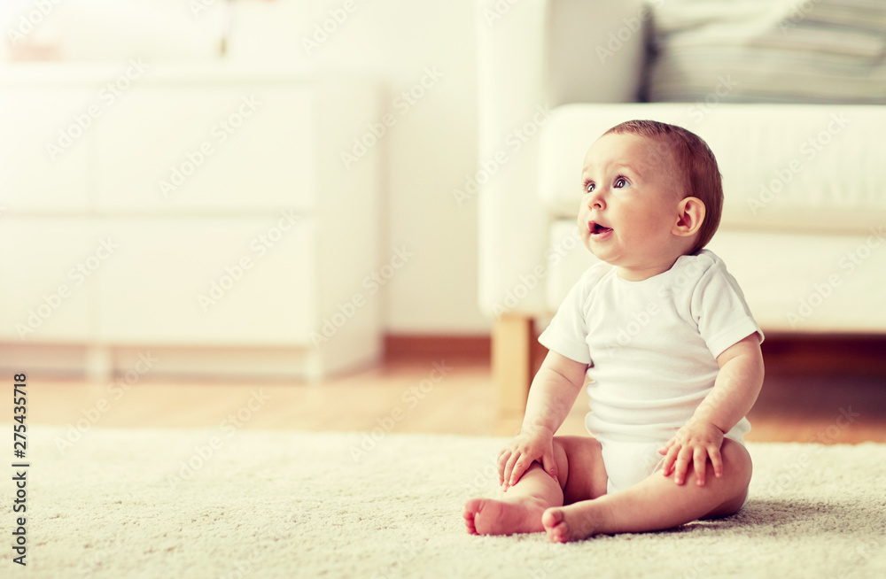 childhood, babyhood and people concept - happy little baby boy or girl sitting on floor at home childhood, babyhood and people concept - happy little baby boy or girl sitting on floor at home