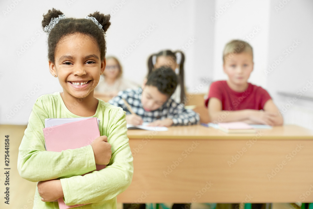 Happy schoolchild standing in classroom, holding books. Happy schoolchild standing in classroom, holding books.